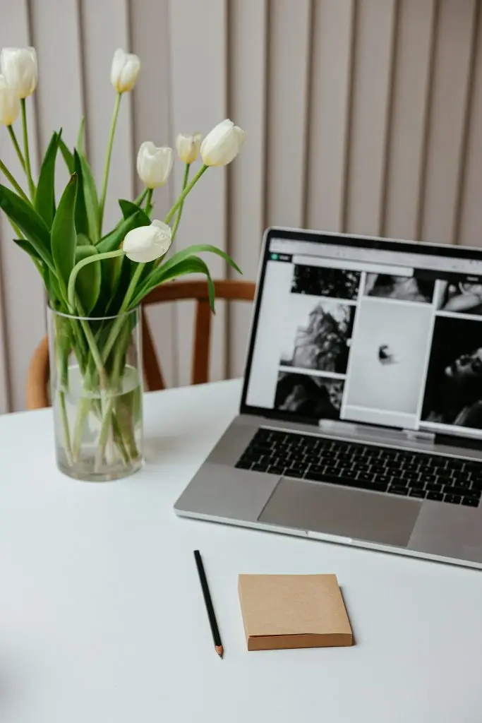 Cozy workspace featuring a laptop, pencil, notepad, and a vase of blooming white tulips on a modern desk.